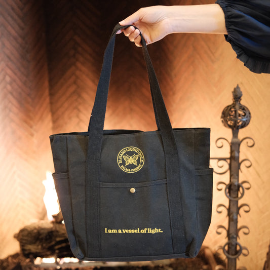 Black bag with gold text and logo held by a hand against a warm-toned background